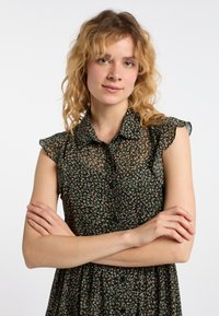 Kwiatowa sukienka w ciemnozielonym kolorze, z krótkimi falbaniastymi rękawami, zapinana na guziki z przodu, o luźnym kroju i rozkloszowanej spódnicy.
