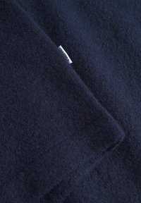 Tengerészkék gyapjú anyag, puha tapintással, a sarkában egy kis fehér címkével. Egyszerű, elegáns dizájn minta nélkül.