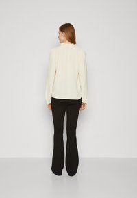 Cream blouse with puffed sleeves, ruffled neckline, paired with black flared pants. Smooth texture and fitted design.