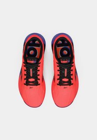 Sapatilhas de treino rosa brilhante com detalhes em preto, atacadores planos, superfície texturizada e um calcanhar roxo. Apresenta a marca "NANO PRO" no interior.