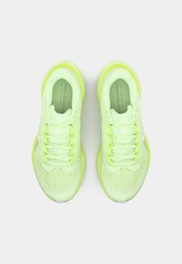 Zapatillas de running de malla verde claro con acentos en neón amarillo, puntera redonda y seis ojales para los cordones. Presentan un logo blanco en el lateral.