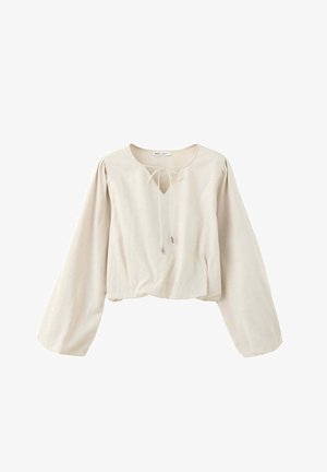 Blouse beige à manches longues avec col rond et lien à nouer, présentant des manches légèrement bouffantes et une coupe ample.
