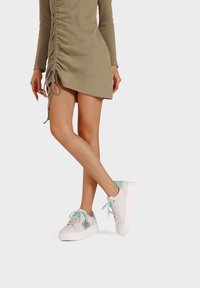 Sneaker bianca con dettagli azzurri chiari e dettaglio grigio testurizzato, con chiusura a lacci e suola spessa. L'outfit include un vestito aderente e arricciato.