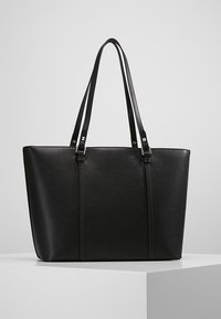 Černá taška přes rameno s pevnou konstrukcí, vyrobená z texturovaného syntetického materiálu, s dvěma dlouhými uchy a stříbrnými kovovými detaily.