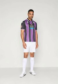 Mörklila och svart randig fotbollströja med krage, med en logotyp på bröstet. Matchas med vita shorts och strumpor.