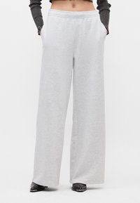 Ανοιχτό γκ ρι παντελόνι φόρμας σε φαρδιά γραμμή με ελαστική μέση, πλαινές τσέπες και μαλακή υφή. Συνδυασμένο με μαύρα υποδήματα.