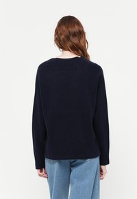 Pullover blu navy realizzato in morbido tessuto a maglia. Presenta un colletto rotondo a coste e polsini, con un fit rilassato e un orlo leggermente accorciato.