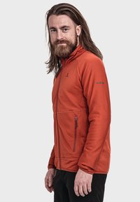 Herren-Fleecejacke in Orange mit hohem Kragen, strukturiertem Muster, seitlichen Reißverschlusstaschen und einem Logo am Ärmel. Glatte Stoffoberfläche.