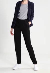 Námořnický sako, šedé tričko a černé kalhoty doplněné bílými teniskami. Sako má přiléhavý střih, kalhoty mají hladkou texturu.