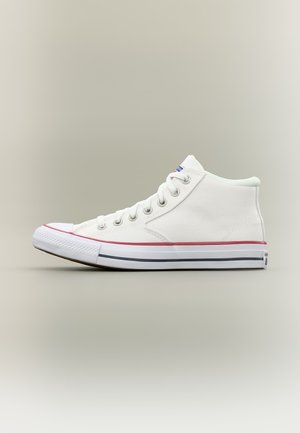 Baskets montantes en toile blanche avec des lacets blancs, rayures rouges et noires sur la semelle, vues de côté sur un fond neutre.