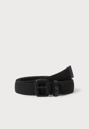 Cinturón negro de tejido trenzado, con una hebilla negra y un pequeño emblema dorado de laureles en la trabilla, enrollado sobre un fondo claro.