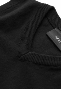 Maglione nero con collo a giro e dettagli a coste. Tessuto morbido e un'etichetta sul lato con il nome del marchio "NEXT."