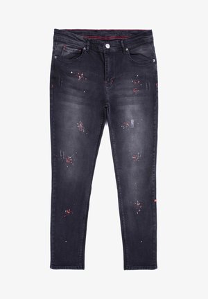 Jean en denim noir avec une coupe slim, présentant des zones usées, des éclaboussures rouges et blanches, ainsi qu'un design traditionnel à cinq poches.