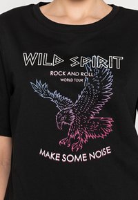Svart bomull t-shirt med korta ärmar som har en flerfärgad grafik av en örn och texten: "WILD SPIRIT ROCK AND ROLL WORLD TOUR MAKE SOME NOISE."