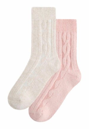 Paket mit zwei Socken: eine cremefarbene und eine pinke. Beide bestehen aus strukturiertem Strickstoff mit Kabelmustern und gerippten Bündchen.