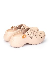 Zuecos de plástico moldeado color beige con orificios de ventilación cortados, correa texturizada y un pequeño buckel marrón como acento. Punta redondeada y suela resistente.