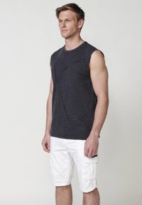 Chemise sans manches en coton gris foncé avec des détails de couture linéaire, associée à un short cargo blanc avec des poches latérales et des ourlets retroussés.