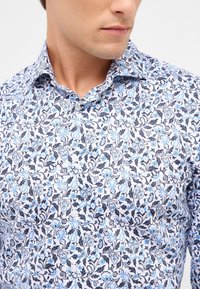 Overhemd met knoopsluiting met een bloemmotief in blauw en zwart op een witte achtergrond, met een gespreid kraag en een soepele textuur.