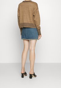 Pull en maille marron avec ourlets côtelés, associé à une mini-jupe en denim bleu à ourlet effiloché, et des mules à talons noires.