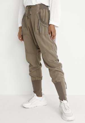 Khaki cargo pants with a drawstring waist, multiple pockets, ribbed cuffs, and textured fabric. Styled with white sneakers.