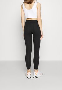 Svarta högmidjade leggings gjorda av ett elastiskt material, kombinerade med en vit kortärmad topp och vita sneakers med orangea detaljer.