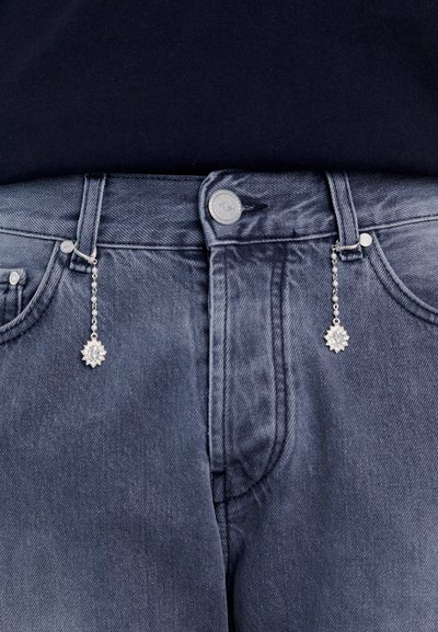 Jeans de ganga escura com um encantinho decorativo prateado preso na parte da frente, apresentando um design circular e ligado por uma pequena corrente.