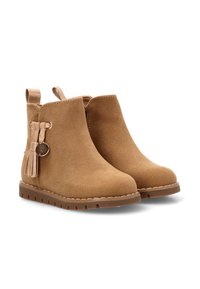 Botas de tobillo de ante marrón con borlas laterales y un acento circular. Cuentan con una suela de goma plana y una lengüeta para ponerlas fácilmente.