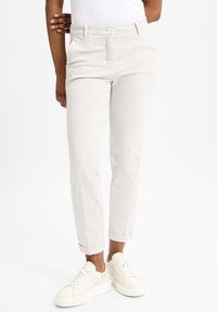 Helle beige, taillierte Hose aus weichem Stoff, mit einem vorderen Knopfverschluss, seitlichen Taschen und gekrempelten Säumen, kombiniert mit weißen Sneakers.