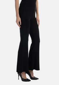 Pantaloni neri a palazzo realizzati in un tessuto elastico, con una vita alta e una texture liscia. Indossati con scarpe con tacco nere.
