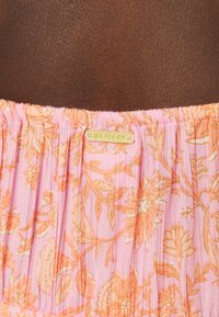 Bas de maillot de bain floral en tissu rose avec des motifs floraux orange, design plissé et détail de label doré "Billabong".