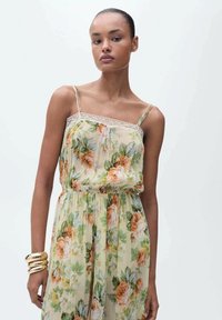 Floral maxi dress in light yellow with green and orange rose patterns; lace trim on adjustable spaghetti straps; lightweight, flowy fabric.