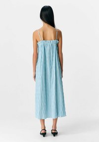 Robe maxi sans manches à rayures bleu et blanc, avec un dos froncé et de fines bretelles réglables, fabriquée en tissu léger.