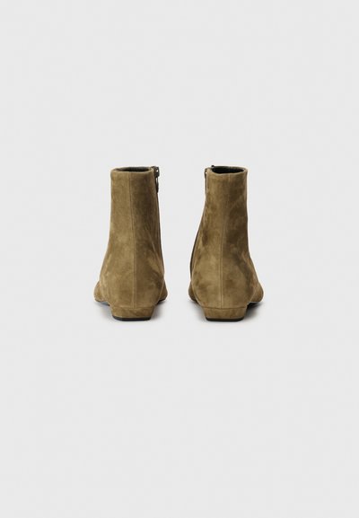Botas de ante marrón hasta el tobillo con una textura suave, forma estrecha y un tacón bajo. Cuenta con una cremallera lateral para facilidad de uso.