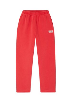 Raudoni sportiniai džinsai, pagaminti iš minkštos medžiagos, turintys elastinį juosmenį ir baltą užrašą "AMERICAN VINTAGE", atspausdintą kairiajame šlaunyje.