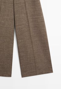 Pantalon en tissu marron texturé avec jambes larges vu du dessous sur fond blanc.