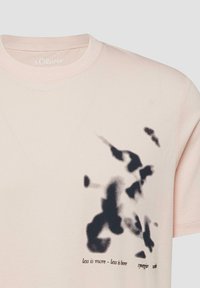T-shirt rose clair avec un motif abstrait en taches d'encre noires et le texte « moins c'est plus - moins c'est ennuyeux » sur le côté droit avant.