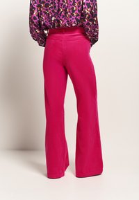 Pantaloni a zampa d'elefante in corduroy fucsia con righe verticali e vita alta, abbinati a una blusa nera e rosa con motivo.