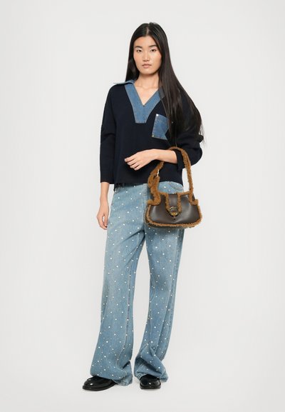 Maglione navy con colletto in denim e tasca, abbinato a jeans a gamba larga azzurri chiari con pois bianchi. Borsa marrone con tracolla testurizzata.