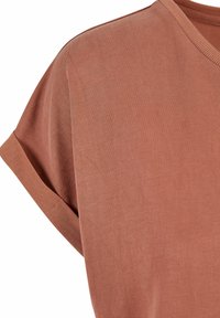 Gros plan d'une chemise marron terracotta à manches courtes avec un revers de manche plié et un col en V côtelé sur fond blanc.