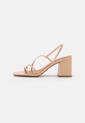 Beżowe sandały na słupku z cienkimi, krzyżującymi się paskami i teksturowaną powierzchnią. Kwadratowy czubek i solidny, wzorzysty obcas dla stabilności.