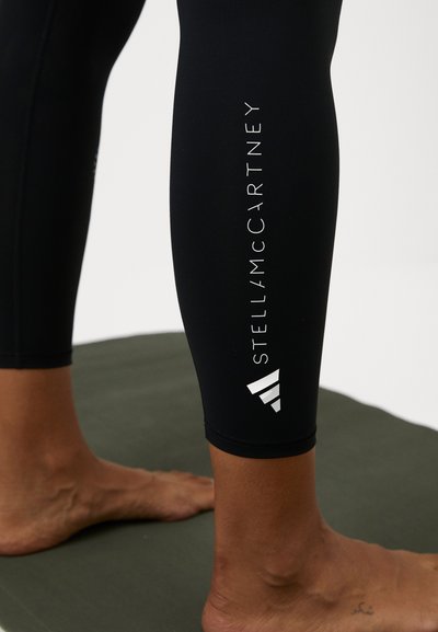 Fekete leggings rugalmas anyagból, fehér "STELLA McCARTNEY" logóval és grafikai elemekkel a szegély közelében.