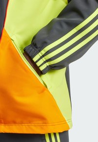 Kleurvolle jas met grijze, felgele en oranje panelen. Voorzien van elastische manchetten en zijzakken met rits en contrasterende stiksels.