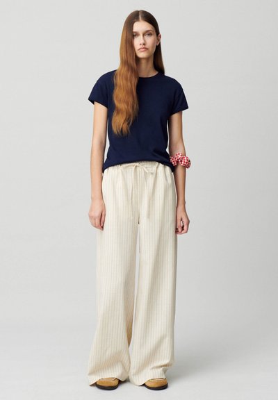 T-shirt navy a maniche corte abbinato a pantaloni a gamba larga beige a righe e mocassini marroni. Capelli pettinati lisci, con uno scrunchie a scacchi rossi.