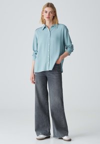Lichtblauwe overhemd met lange mouwen, gedragen met high-waisted donkergrijze rechte jeans en witte sneakers. Eenvoudig, schoon ontwerp.
