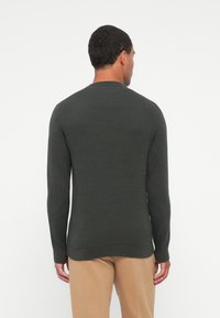 Pull en maille vert foncé avec un col rond, des manches longues et un ourlet côtelé. Texture lisse et coupe ajustée.