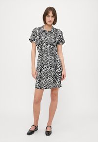Crna i bijela haljina s kratkim rukavima i apstraktnim uzorkom lista, uz uski struk i dugmad s jedne strane. Glatka tekstura tkanine.