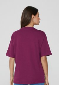 Camiseta de manga corta y cuello redondo de algodón en un tono púrpura intenso. Presenta un ajuste holgado y una textura suave con un diseño sencillo.