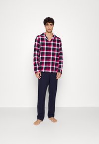 Kariertes Hemd mit Button-Up in Rosa, Weiß und Marineblau, kombiniert mit dunkelblauen Hosen. Das Hemd hat einen Kragen und lange Ärmel.