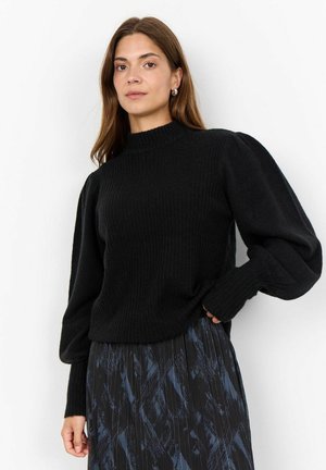 Maglione nero a coste con colletto alto e maniche a palloncino, abbinato a una gonna a pieghe con motivo in tonalità scure.