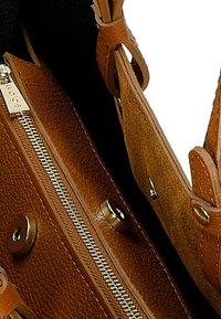 Brązowa skórzana torebka o teksturowanym wykończeniu, z widocznym zamkiem błyskawicznym i metalowymi detalami. Posiada zamszowe wnętrze i akcenty dekoracyjne.